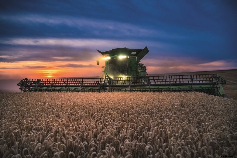 John Deere X9 combine harvesting wheat at night in Europe